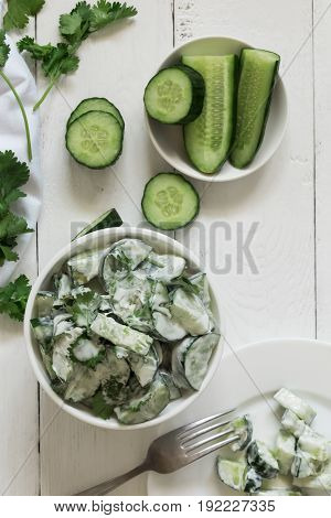 Cucumber salad with coriander and yogurt dressing on the white wooden background. Top view