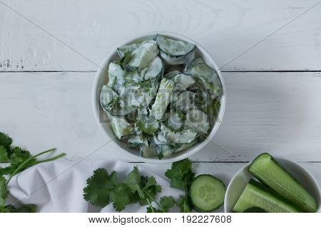 Cucumber salad with coriander and yogurt dressing on the white wooden background. Toned photo