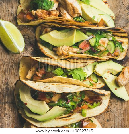 Tacos with grilled chicken, avocado, fresh salsa and limes over rustic wooden background, top view, square crop. Healthy low carb and low fat lunch or food for company. Dieting or weight loss concept