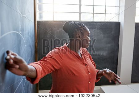 Focused and confident young African businesswoman giving a presentation to unseen colleagues while writing on a chalkboard in a modern office