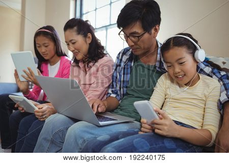Family using laptop, digital tablet and mobile phone in living room at home