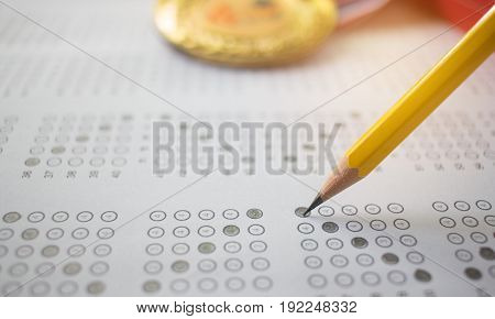 yellow pencil on exam answer sheet with medals blur background education test and winner concept