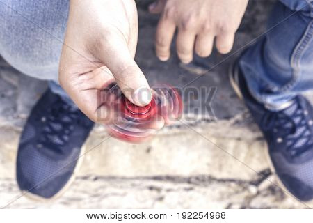 Closeup of a young caucasian man playing with a red fidget spinner on a concrete background. Popular spinner gadget in 2017.