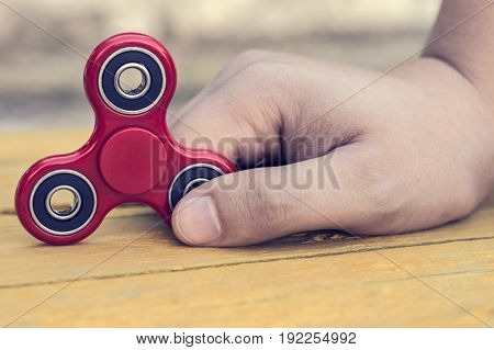 Caucasian man holds his finger (hand) Red fidget spinner in motion stress relieving toy on on a yellow wooden background