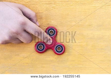 Caucasian man holds his finger (hand) Red fidget spinner in motion stress relieving toy on on a yellow wooden background