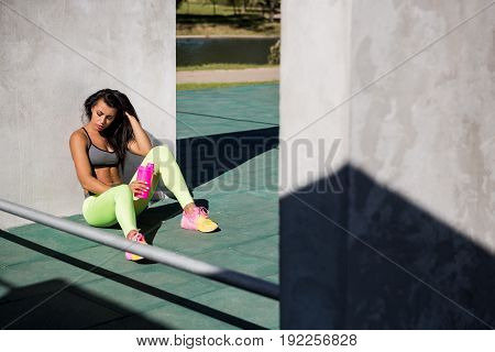Beautiful young girl with long legs in bright sexy leggings with pretty athlete muscular body sit with protein shaker. Cross training urban area street gym city exercise routine healthy lifestyle.