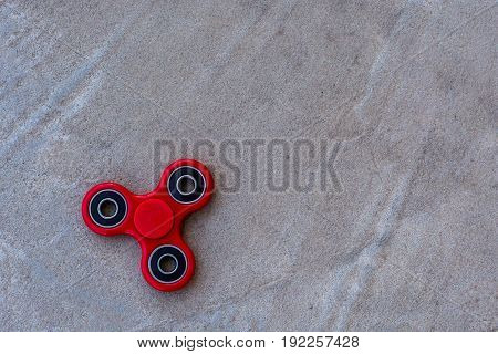 Red fidget spinner in motion stress relieving toy on concrete background.