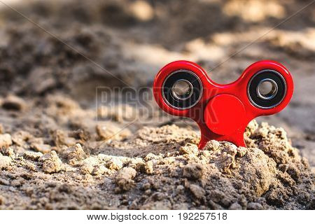 Popular red spinner gadget in 2017 against the background of sand. Modern red plastic spinner fidget game for young people.