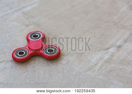 Red fidget spinner stress relieving toy on concrete background.
