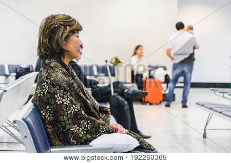 Woman waiting seated on the airport's departure lounge for her flight with some blurred people on background.