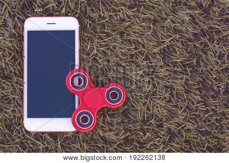 Top view of the popular spinner gadget in 2017 and a white mobile phone (smartphone) on a green artificial lawn