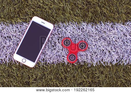 Top view of the popular spinner gadget in 2017 and a white mobile phone (smar tphone) on a green and white artificial lawn
