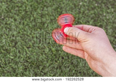 Closeup of a young caucasian man playing with red fidget spinner on f the soccer (football) artificial field. Popular gadget in 2017