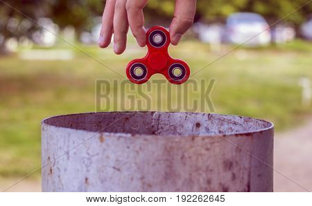 Closeup of a young caucasian man throwing a red fidget spinner in a garbage can on the background of nature. Popular spinner gadget in 2017.
