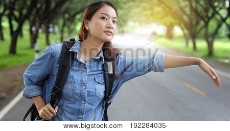 Asian women tourists and backpackers waiting car and Freedom traveler woman standing with raised arms at the roadside.