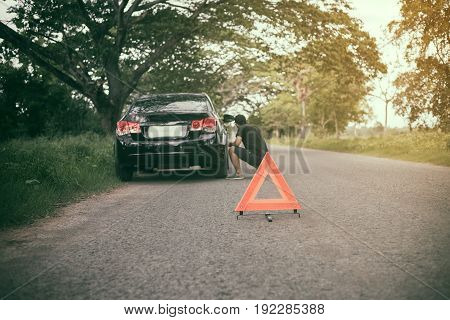 Stressed man sitting after a car breakdown with Red triangle of a car on the road