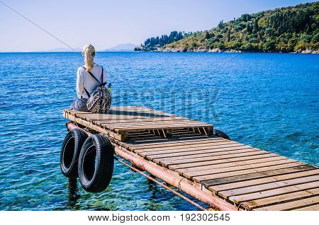 Girl with backpack on pier on the beach near Kalami looking into sea. Corfu Island, Greece.