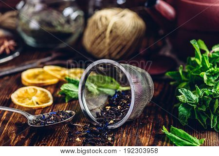 Dry Tea in Strainer and Spoon with Fresh Mint Bunch and Lemon Slices. Tangle with Two Jars and Teapot on Backdrop.