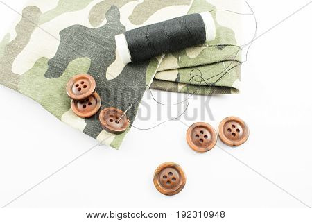 Still life composed of thread cloth needle and buttons. White background.