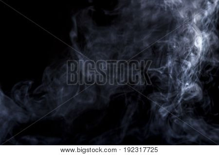 Smoke from a Vape with light effects on a black background. The image is an abstract texture with copy or text space. It has patterns showing movement and depicts a spooky mood with a Halloween theme.