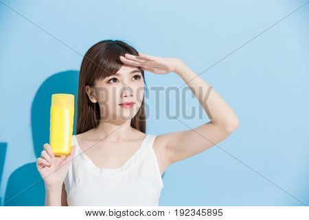 woman take sunscreen and look somewhere on blue background