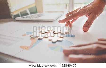 Asian business woman hands on a wooden office desk pick puzzle. Business solutions success and strategy concept. Businessman hand connecting jigsaw puzzle.Close up photo with selective focus.