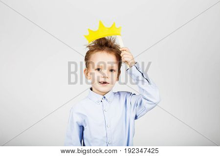 Portrait Of A Cute Little School Boy With Yellow Paper Crown Against A White Background.