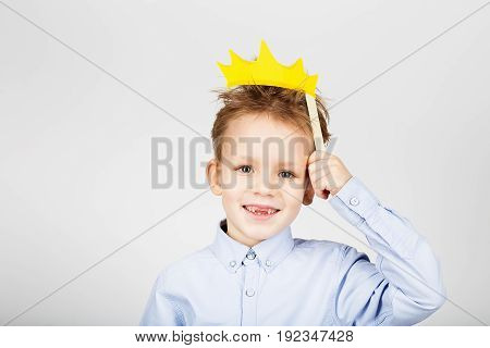Portrait Of A Cute Little School Boy With Yellow Paper Crown Against A White Background. Cheerful Sm