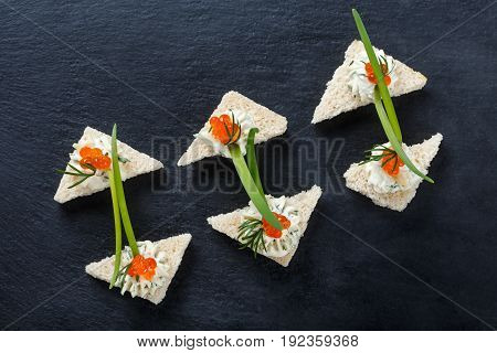 Appetizer canape with red caviar and cream cheese on stone slate background close up. Delicious snacks sandwiches crostini brushetta antipasti on party or picnic time. Top view