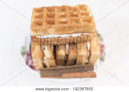 Viennese waffles with cream filling and one stick of cinnamon lie on a white saucer with a floral pattern in the defocus on a white background