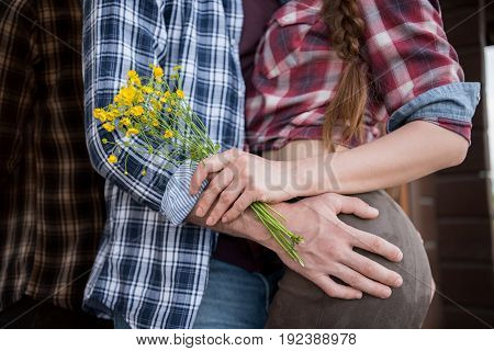 cropped view of passionate couple embracing while woman holding yellow flowers