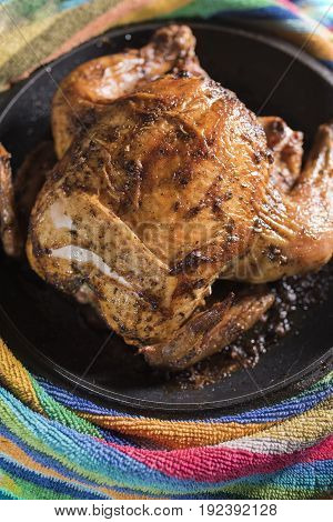 Fried fat chicken lays in a black frying pan on a multi-colored striped background a vertical frame.