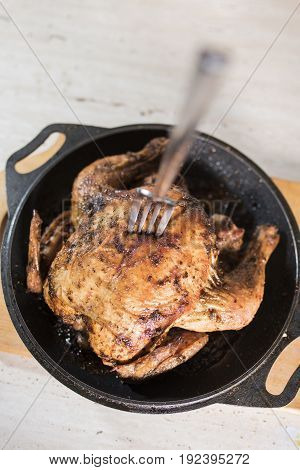 Fork in defocus in fried chicken grill on a black frying pan on a light wooden board