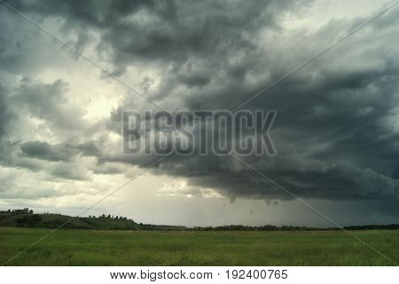 Storm cloud over green fields and hills.