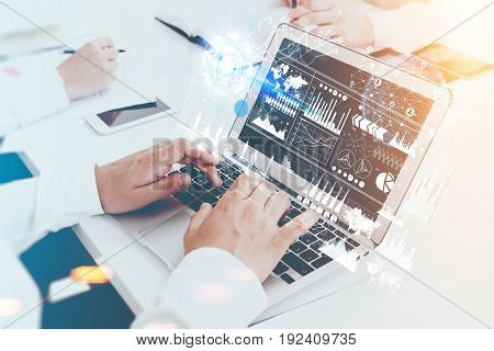 Close up of hands of an unrecognizable businessman. He is typing at his laptop keyboard. Graphs and holograms in the air. Toned image double exposure.