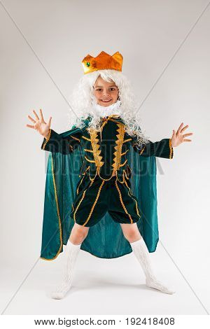 Little curly king stands legs apart and hands. Grey background.