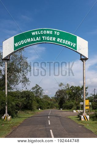 Nilgiri Hills India - October 26 2013: Mudumalai Tiger Reserve sign along road in Masamigulli Forest. Sign as gate over asphalted road. Blue sky and green vegetation.