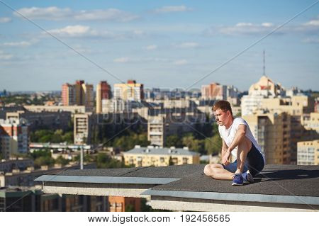 Roofer on the edge of the roof. A man is looking away from a high-rise building. Courage and adrenaline. Roofing
