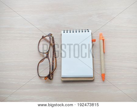 wood table with blank screen for text on notepad paper pencil and modern eyeglasses view from top wood table.