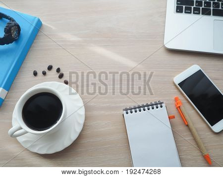 wood office table with hot black coffee cup blank screen on notebook paper and pencil pink heart shape sign cell phone. view from front office table.