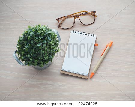 wood office table with small tree on pot modern eyeglasses and blank screen on notepad paper. view from top office table.