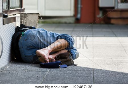 Homeless man sleeps on the street, in the shadow of the building. Social documentary street.