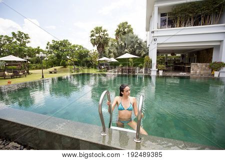 Smiling young Caucasian woman wearing bikini climbing out of outdoor hotel pool at summer resort