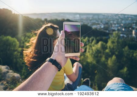 woman with man sitting on the top of the hill injoy view, first person view, man taking picture of woman on sunset