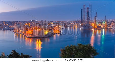 Panoramic aerial skyline view of ancient defences of Three cities, three fortified cities of Birgu, Senglea and Cospicua and Grand Harbor with ships, as seen from Valletta during morning blue hour, Malta.