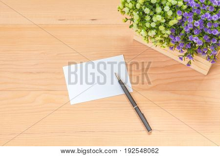 Paper note with pen and flowers on wood background
