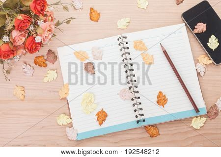 Spiral notebook with phone and maple leaves on wood background in autumn