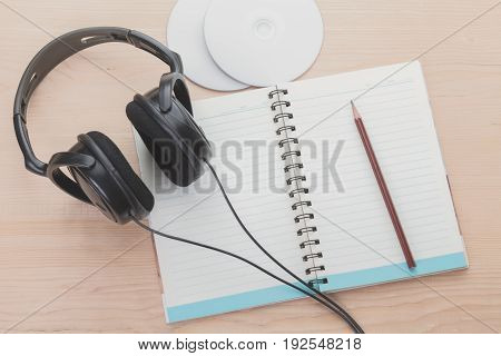 Spiral notebook with pencil headphone and music disc on wood background