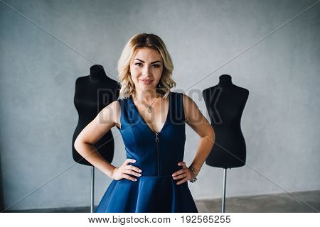 Woman fashion designer in a blue dress is standing near the mannequins. Lips with injection