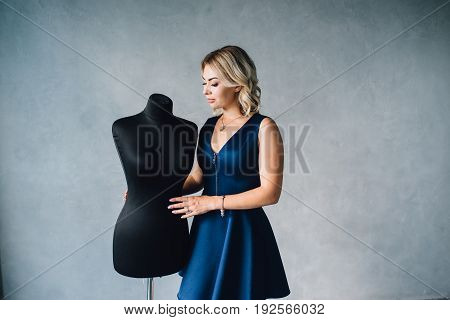 Woman fashion designer in a blue dress is standing near the mannequins. Lips with injection